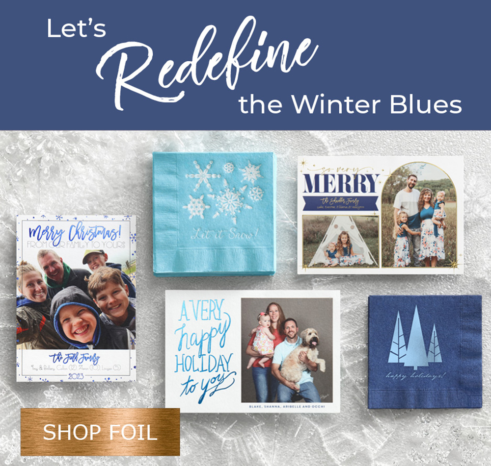 Custom photo holiday cards with different shades of blue foil are laid out on a frosty backdrop.