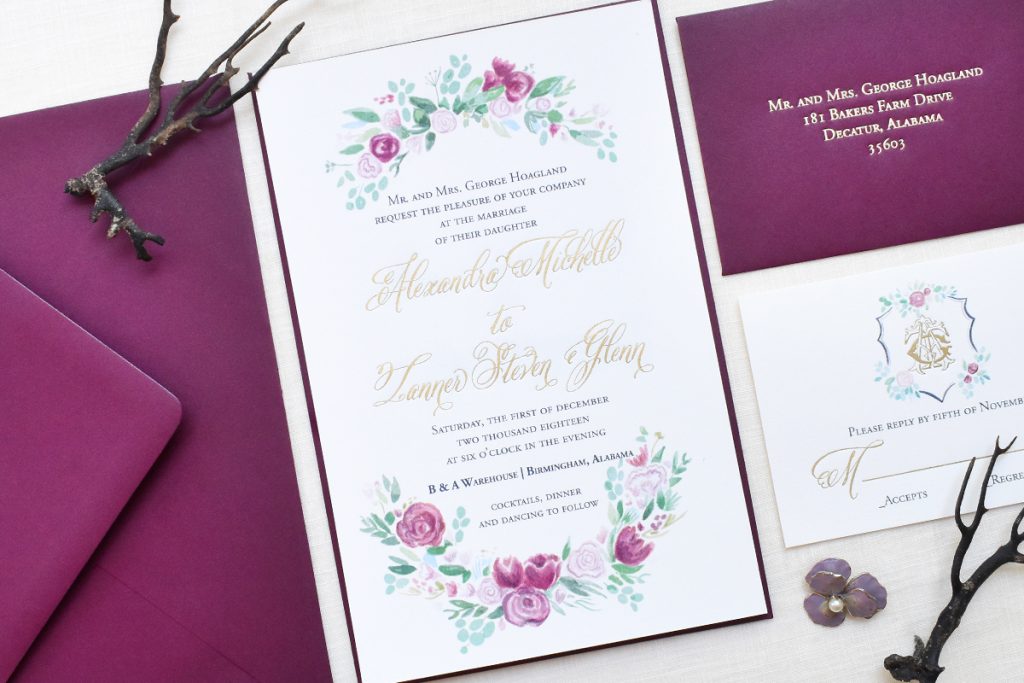 A wedding invitation with bright purple floral accents and a unique crest on the response card.