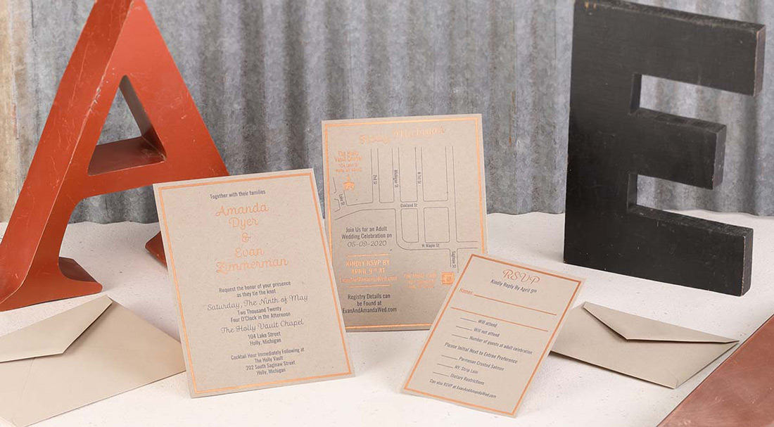 A custom wedding invitation suite on kraft paper with copper foil accents is arranged with wooden letter accents. 
