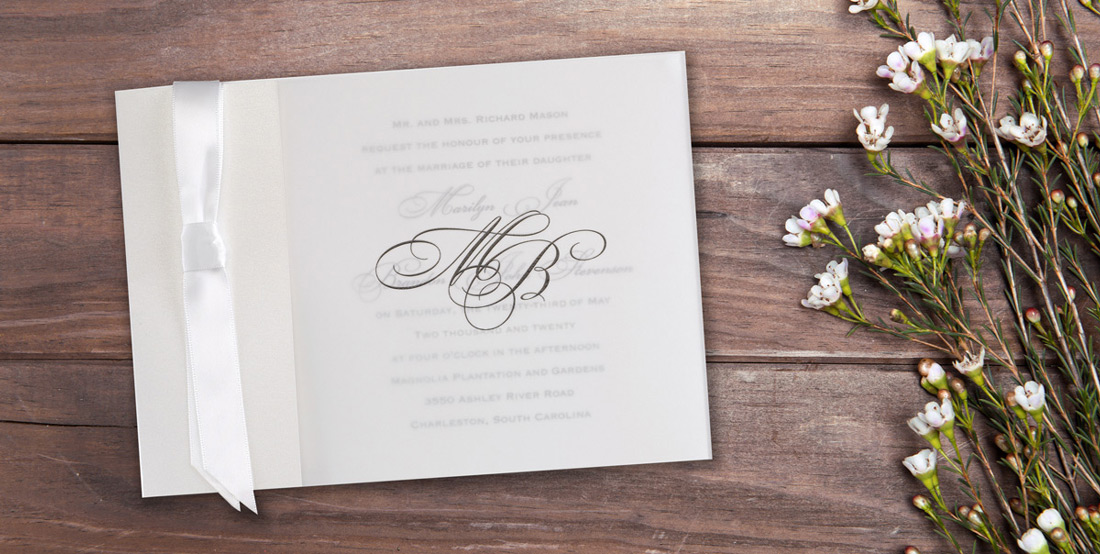 Wedding invitation with translucent vellum overlay custom printed with a monogram next to a floral accent.