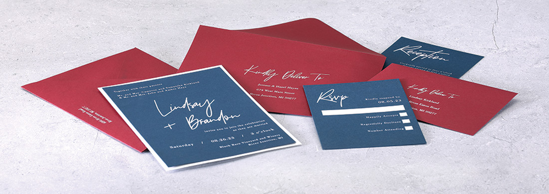 A navy blue invitation with white ink is placed on top of a red envelope also featuring white ink printing.