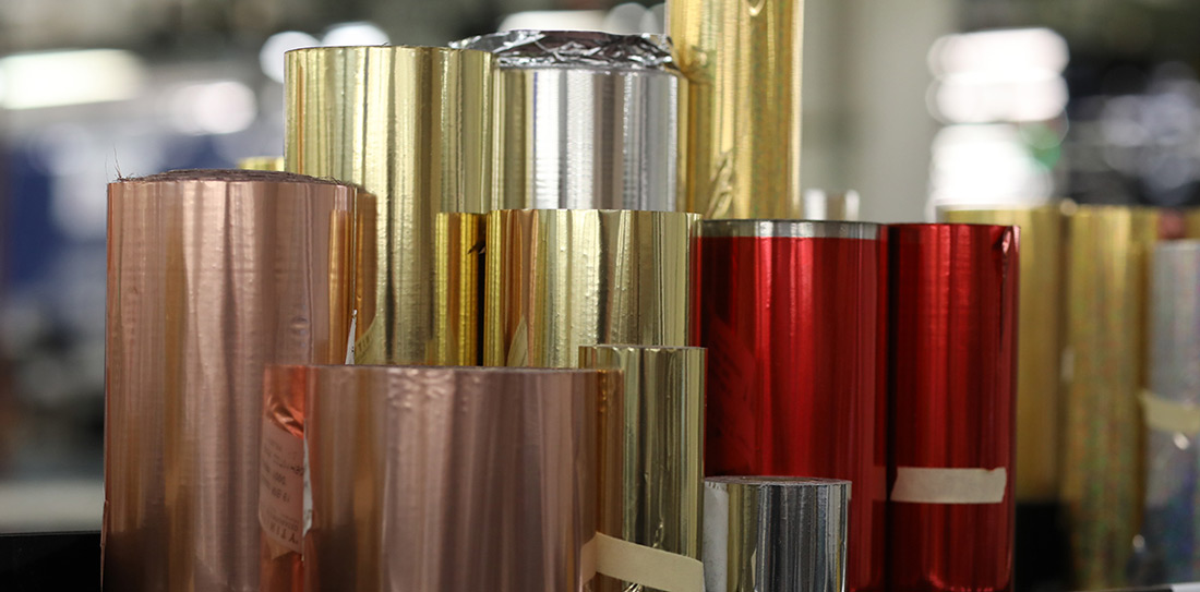 Rolls of gold foil stacked next to each other creating a shimmering formation of pink, gold, silver and red. 