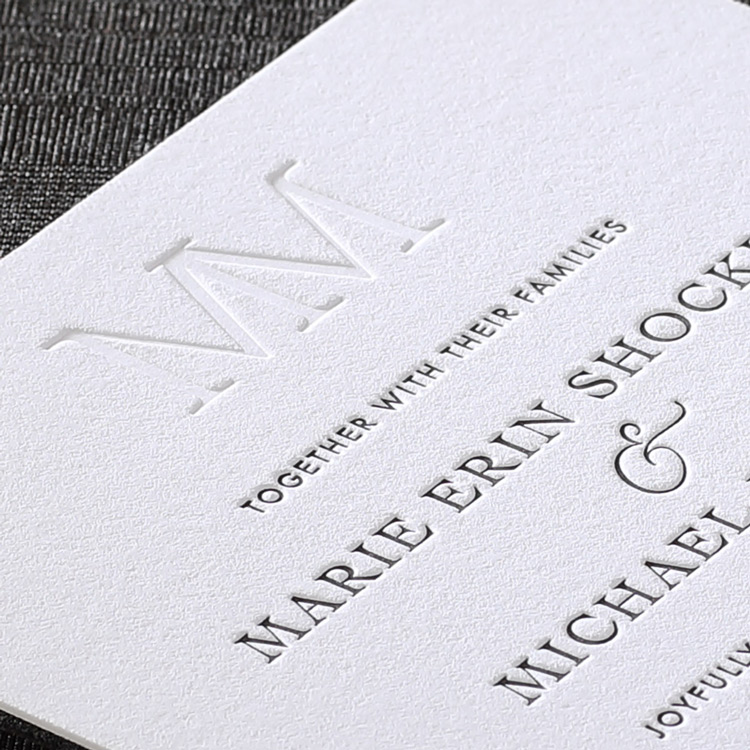 A closeup showing the depth and detail of the blind embossed monogram on this custom wedding invitation. 