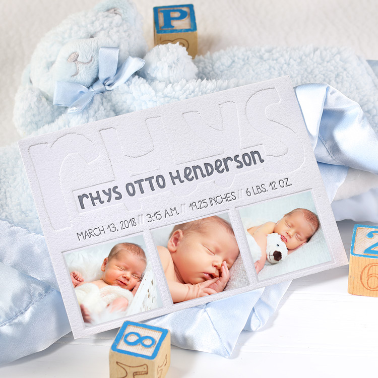 A birth announcement featuring blind letterpress with spots for photos is propped against a light blue baby blanket and accented with toy blocks. 