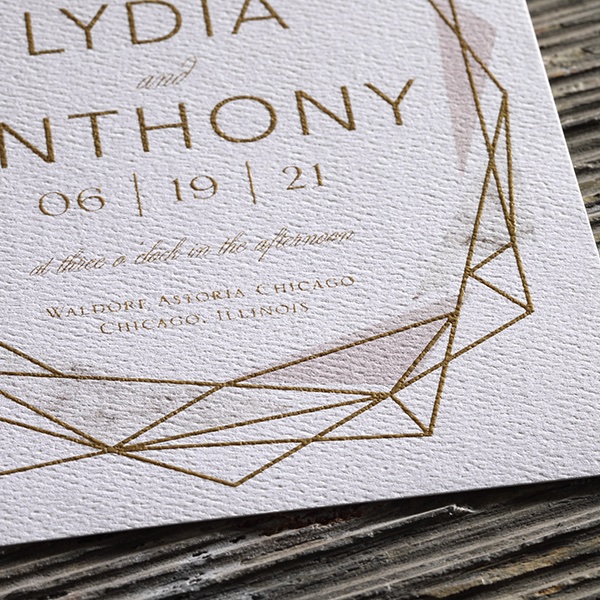 A custom wedding invitation with geometric design in gold thermography ink and watercolor pattern accent design. 