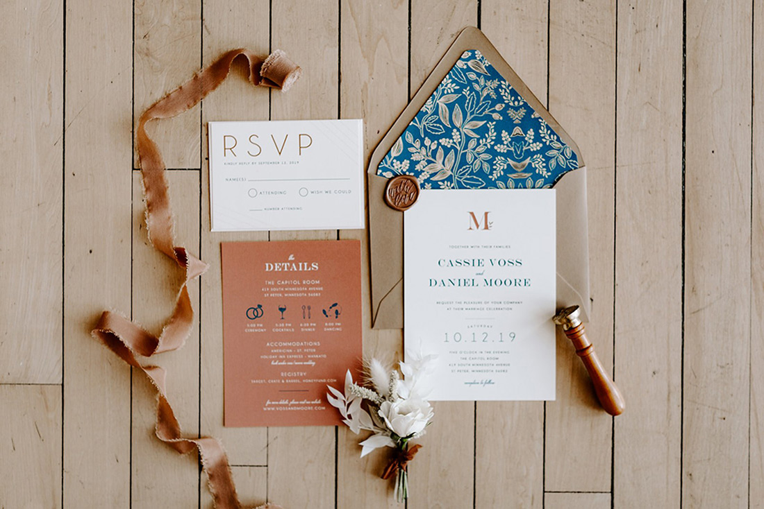 A colorful wedding invitation suite against a beat board background with accent ribbon and a traditional wax seal. 