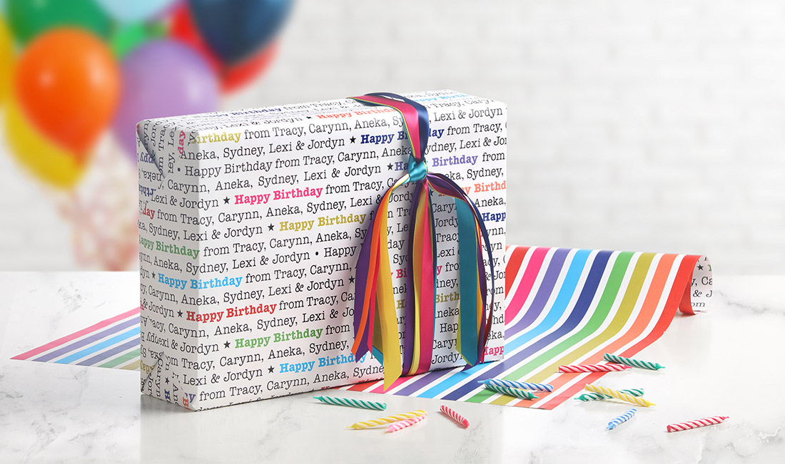 A gift is wrapped in personalized birthday wrapping paper with a colorful arrangement of satin ribbon to match. 