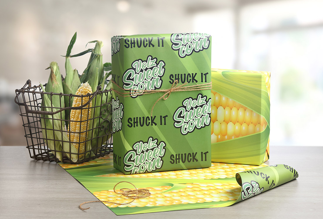 A gift is wrapped in custom wrapping paper for a corn business. The design says "shuck it" next to the business logo.