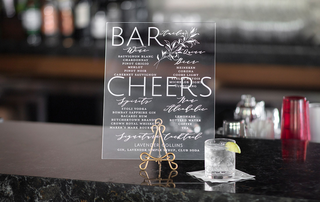 A custom acrylic bar sign is printed with the bar menu and displayed on a granite counter top. 