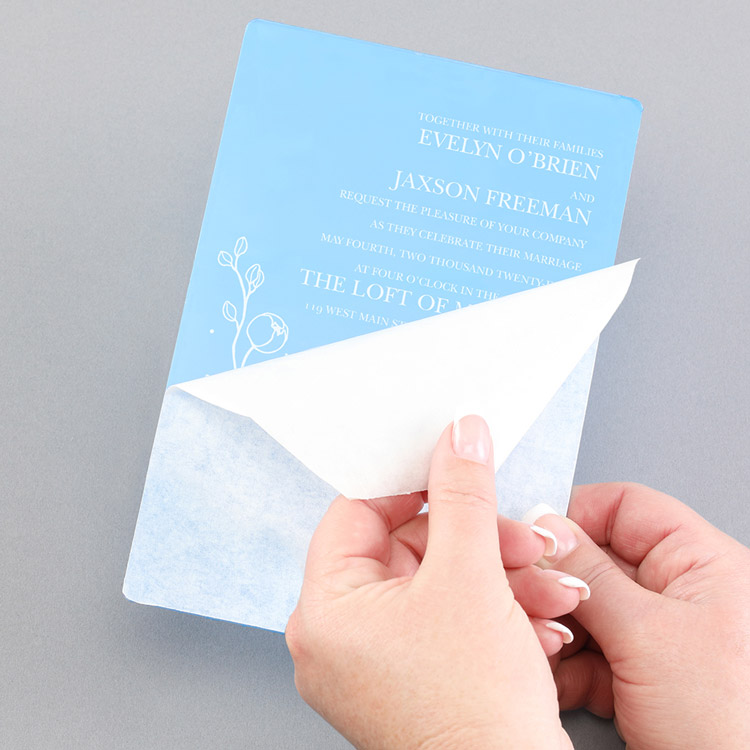 The protective layer on an acrylic piece is shown being pulled back and revealing the wedding invitation underneath. 