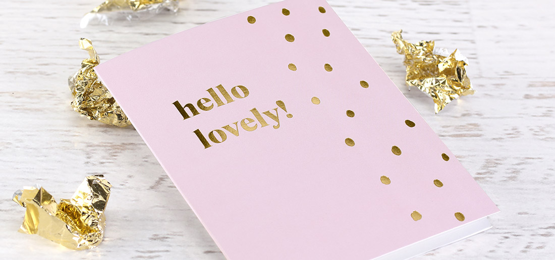 A pink greeting card is foil stamped with "hello lovely" and polka dots. 