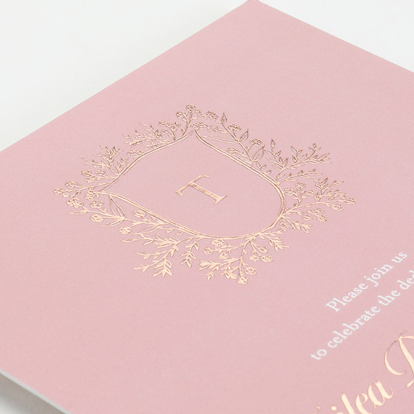 A foil-stamped wedding invitation on pink paper with gold foil shining. 