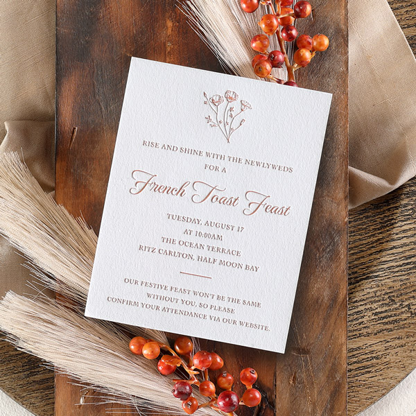 An adorable brunch invitation is printed in letterpress and placed on a rustic backdrop of wood and berries. 