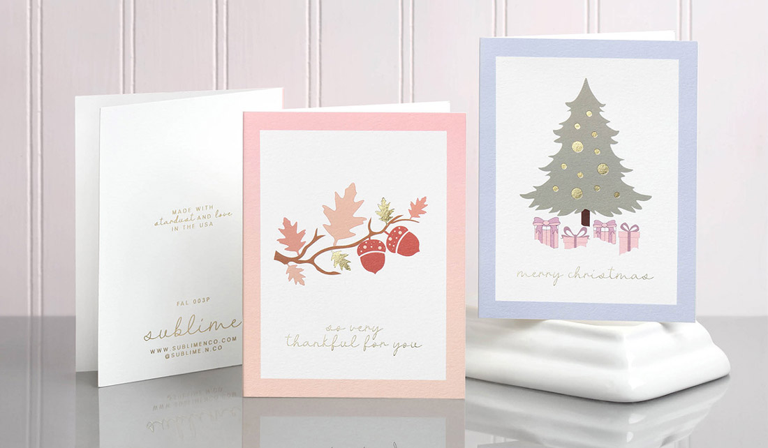Holiday Greeting Cards in soft pastels featuring digital print and gold foil stamping are displayed on a mirrored surface. 