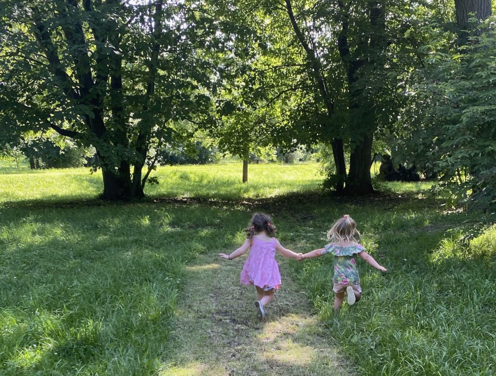 Young girls running hand in hand on a grassy path. 